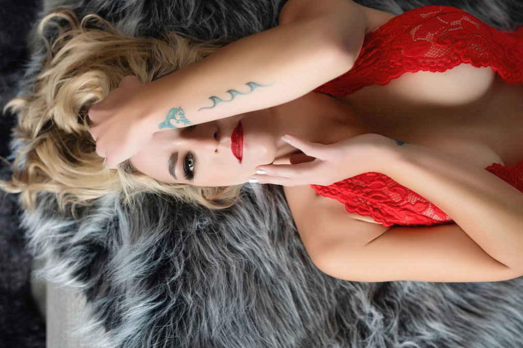 Elegant individual posing on a bed in red lingerie for a boudoir photography session in Tri-Cities Washington.